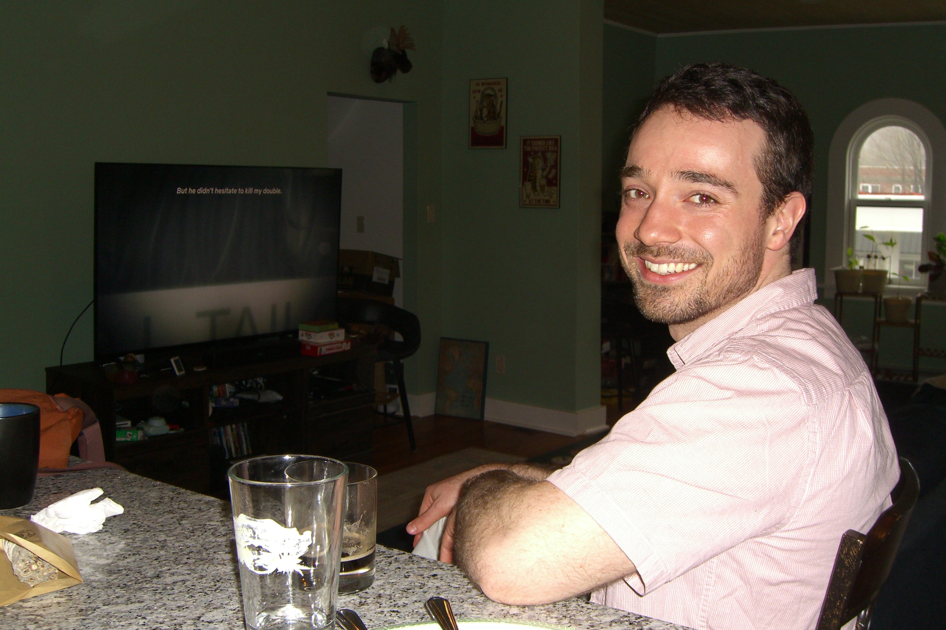 Man sitting at a counter with a glass, TV in background