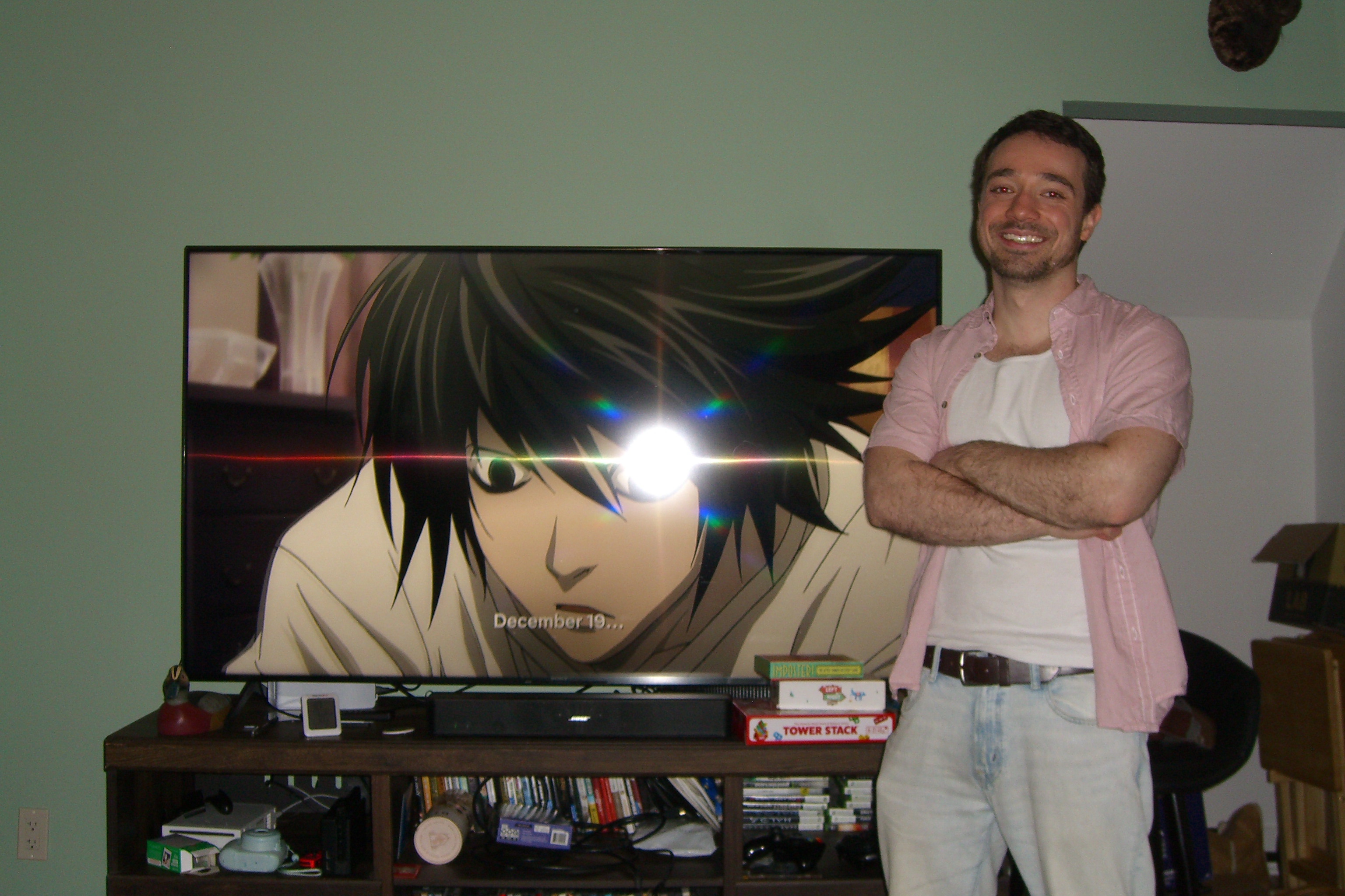 Man smiling next to a TV showing Death Note