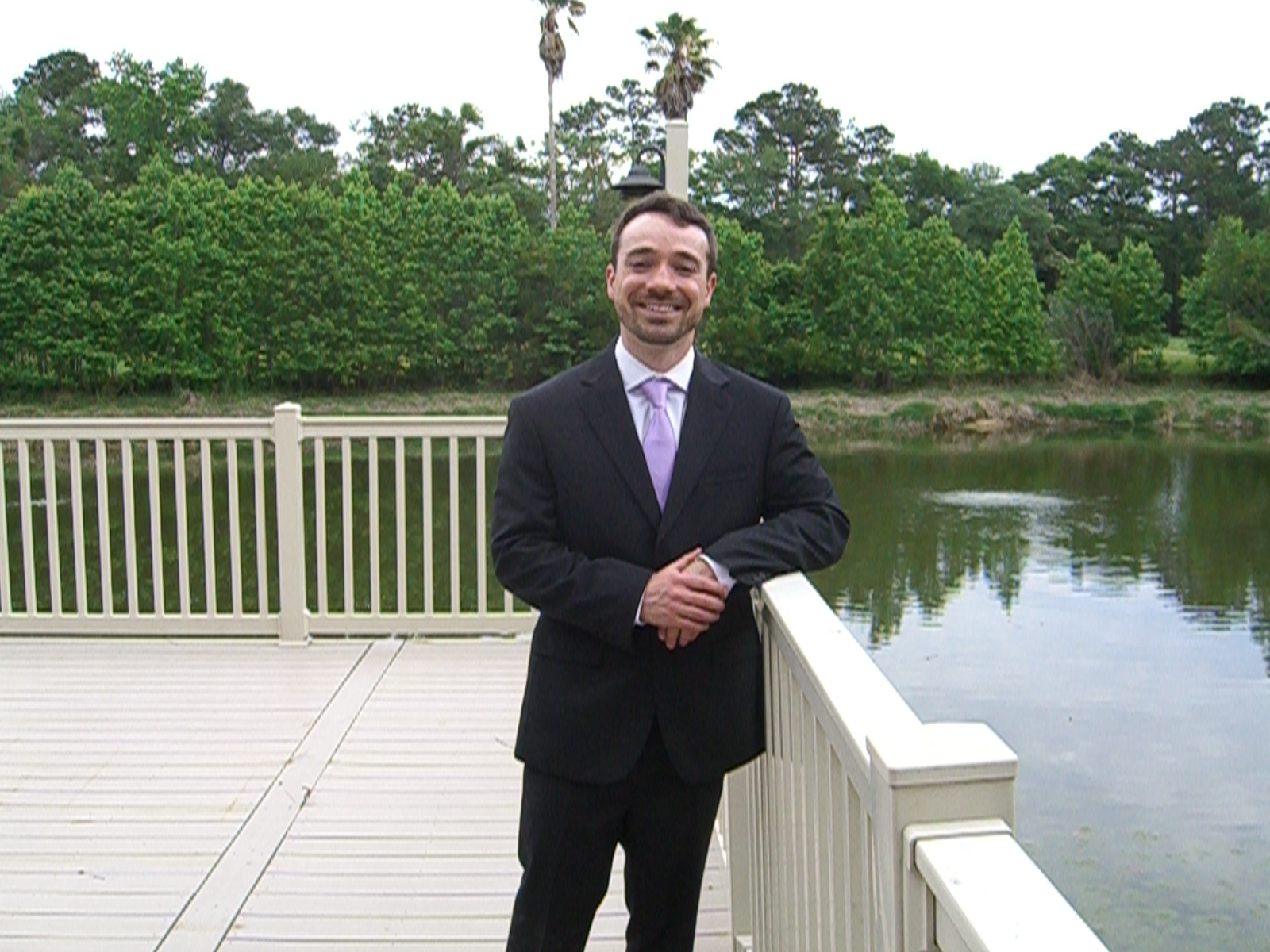 Man in suit standing on a dock in front of a pond
