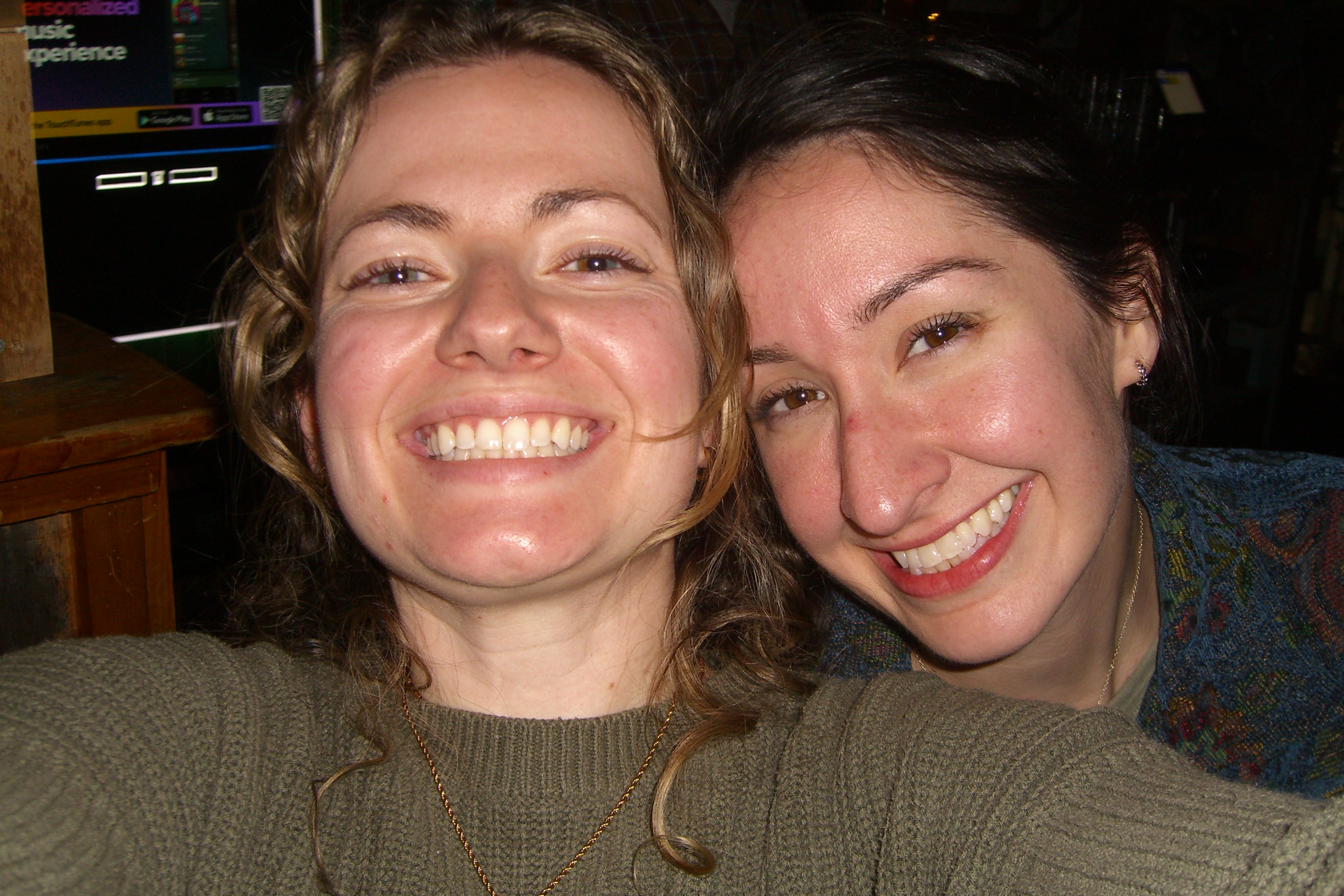 Two women smiling cheek-to-cheek at a bar